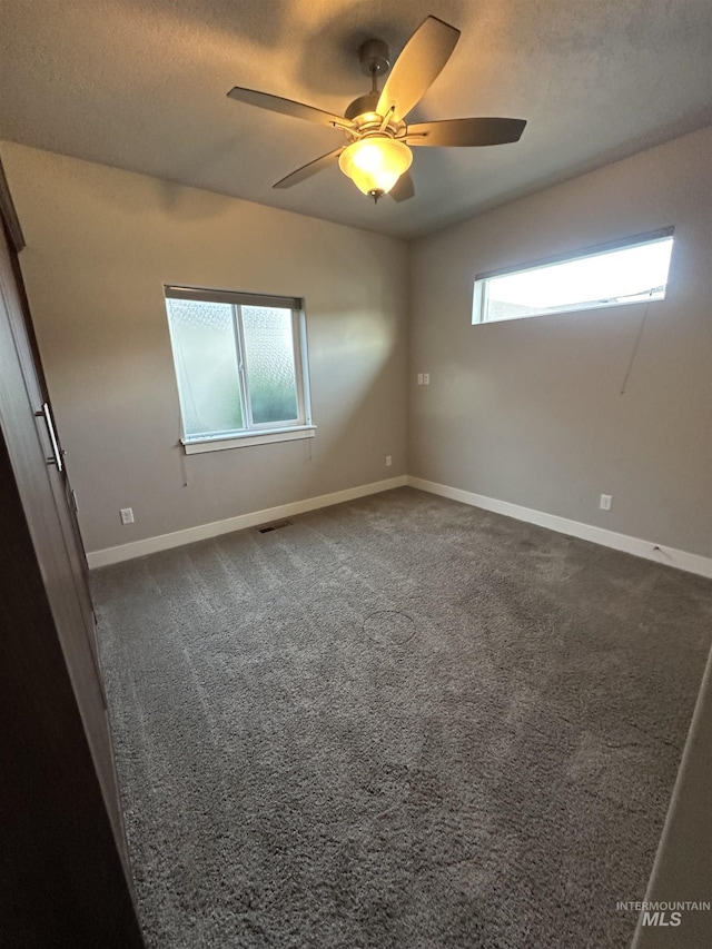 unfurnished room featuring baseboards, a ceiling fan, dark colored carpet, and a textured ceiling