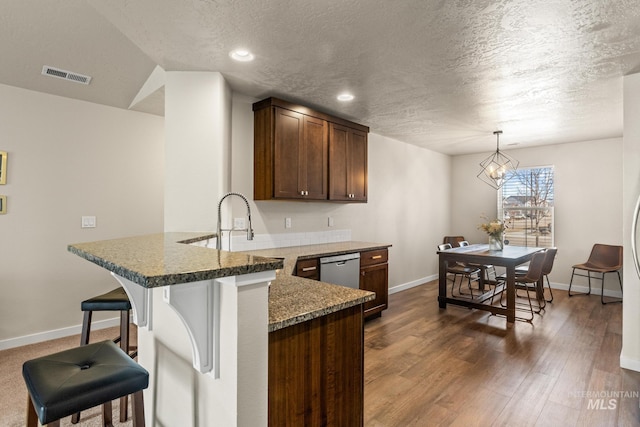 kitchen with visible vents, stainless steel dishwasher, dark wood-style floors, a peninsula, and a breakfast bar area