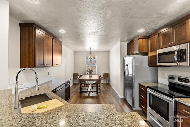 kitchen featuring light stone counters, dark wood-style floors, a sink, stainless steel appliances, and a textured ceiling