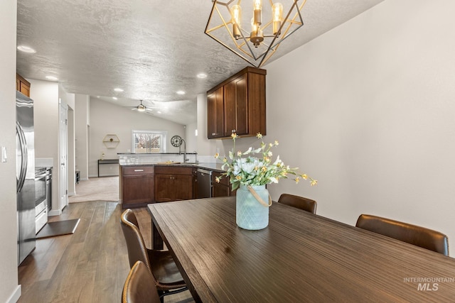 unfurnished dining area with a sink, ceiling fan, vaulted ceiling, a textured ceiling, and dark wood-style flooring