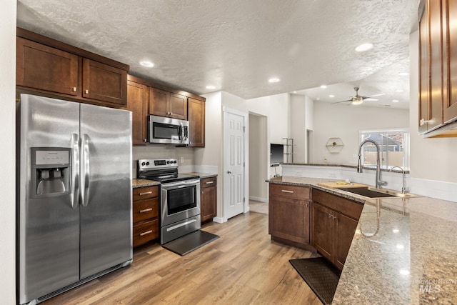 kitchen with light wood-type flooring, light stone counters, a peninsula, stainless steel appliances, and a sink