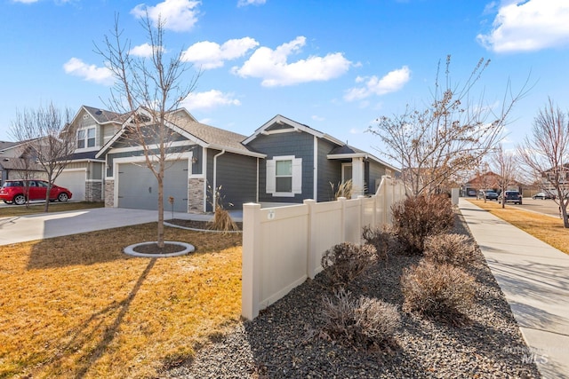 craftsman inspired home with a front yard, fence, an attached garage, concrete driveway, and stone siding