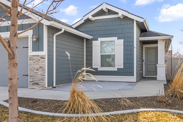 exterior space with stone siding, an attached garage, a shingled roof, and fence