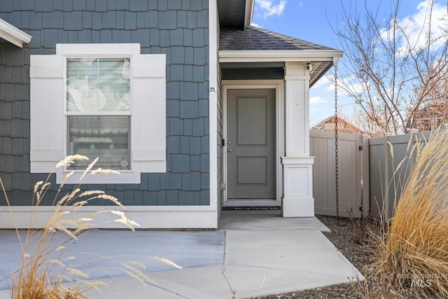 entrance to property with a shingled roof and fence