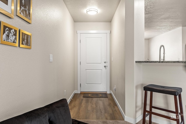 doorway with baseboards, dark wood-style flooring, and a textured ceiling