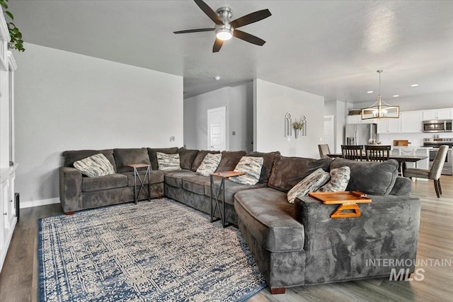 living area with wood finished floors, baseboards, and ceiling fan with notable chandelier