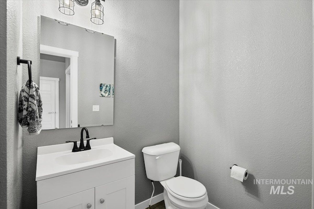 bathroom featuring vanity, toilet, a textured wall, and baseboards