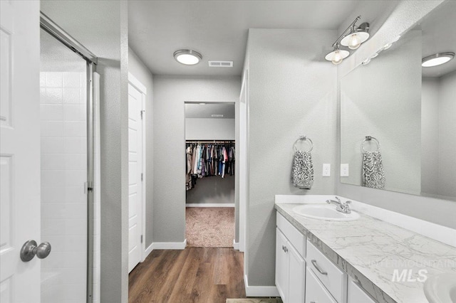 bathroom with a stall shower, a sink, wood finished floors, and visible vents
