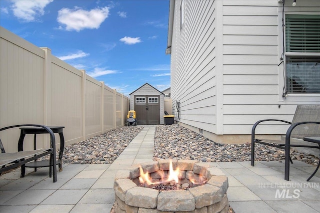 view of patio with an outdoor fire pit, a fenced backyard, a shed, and an outdoor structure