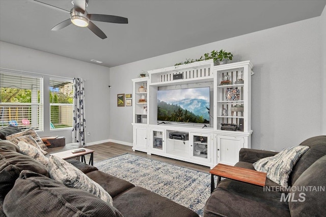 living room with baseboards, visible vents, wood finished floors, and ceiling fan