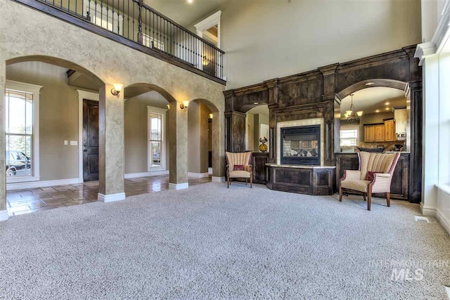 unfurnished living room with light carpet, arched walkways, baseboards, and a towering ceiling