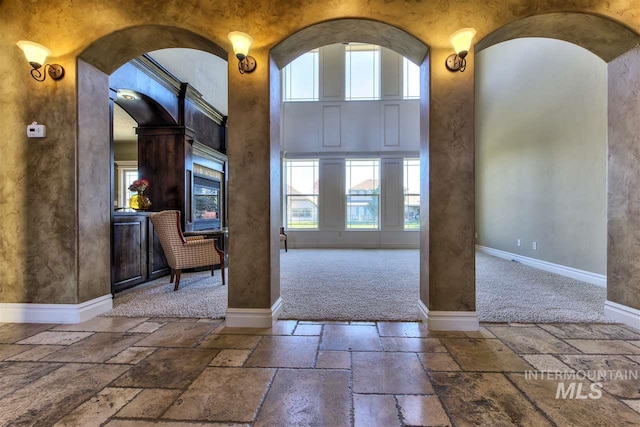 entrance foyer featuring baseboards, arched walkways, stone tile floors, and a healthy amount of sunlight