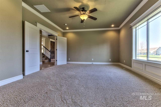 carpeted spare room with visible vents, baseboards, ornamental molding, stairs, and ceiling fan