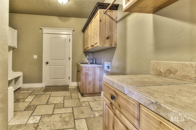 laundry room featuring a sink, stone tile floors, cabinet space, baseboards, and hookup for a washing machine