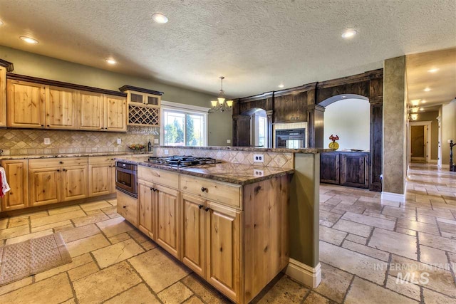 kitchen with a kitchen island, dark stone countertops, appliances with stainless steel finishes, stone tile flooring, and a notable chandelier