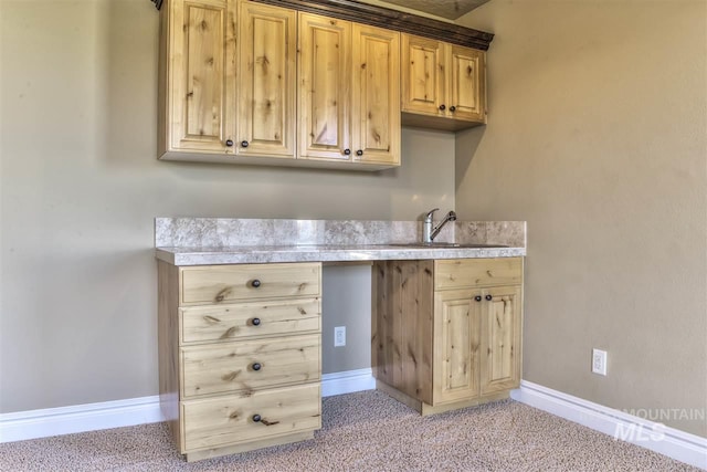 kitchen featuring baseboards, a sink, light brown cabinetry, light countertops, and light carpet