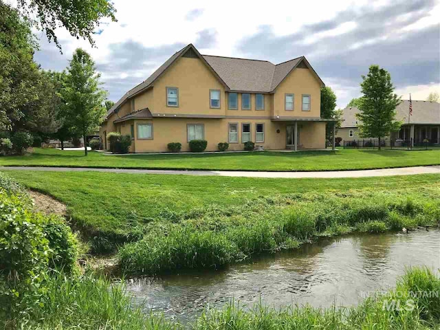 rear view of house featuring stucco siding, a water view, and a lawn