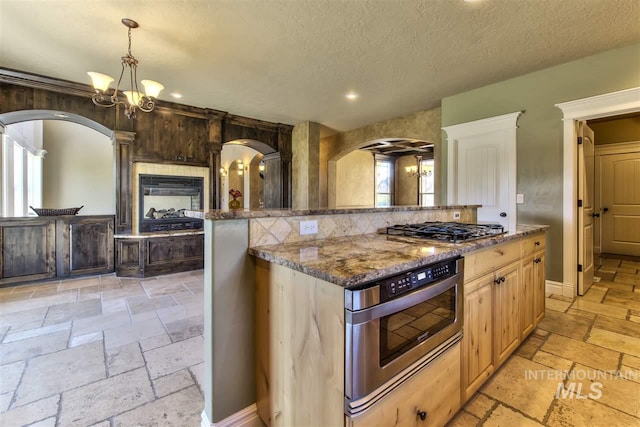 kitchen with stone tile floors, wall oven, dark stone counters, arched walkways, and stainless steel gas cooktop