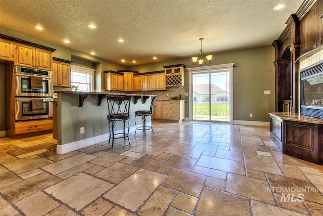 kitchen featuring a breakfast bar area, baseboards, stone tile flooring, double oven, and a chandelier