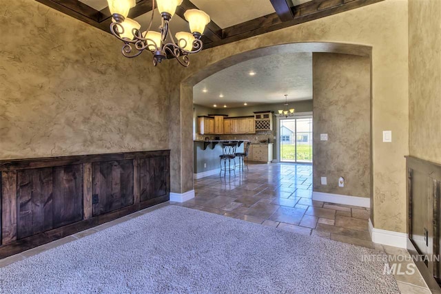 interior space with stone tile floors, baseboards, beam ceiling, arched walkways, and a chandelier