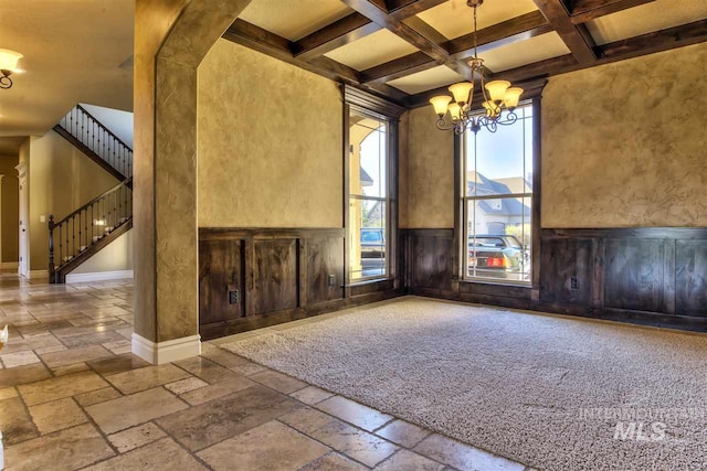 interior space featuring stone tile floors, coffered ceiling, an inviting chandelier, stairs, and wainscoting