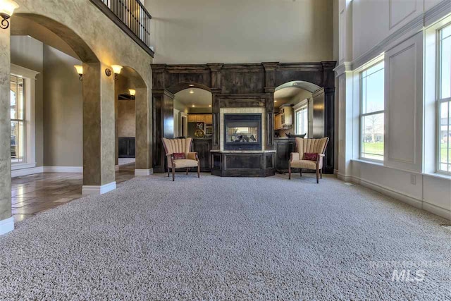 unfurnished room featuring a multi sided fireplace, arched walkways, and a high ceiling