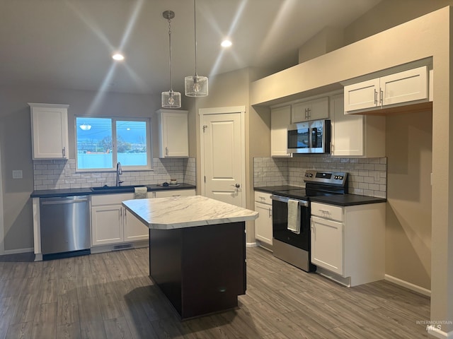 kitchen featuring stainless steel appliances, a kitchen island, decorative light fixtures, and white cabinetry