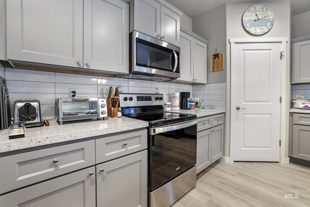 kitchen featuring tasteful backsplash, gray cabinets, light hardwood / wood-style floors, and appliances with stainless steel finishes