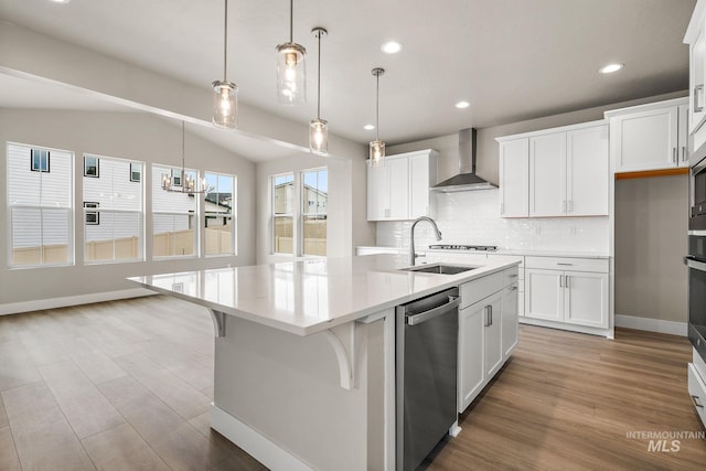kitchen featuring a kitchen island with sink, stainless steel appliances, wall chimney exhaust hood, tasteful backsplash, and a sink