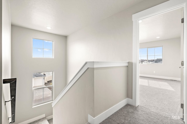 hall featuring baseboards, an upstairs landing, and carpet flooring