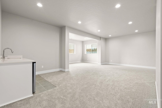 below grade area featuring light carpet, baseboards, recessed lighting, and a sink