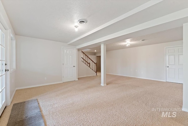 finished below grade area featuring light colored carpet, stairs, baseboards, a textured ceiling, and visible vents