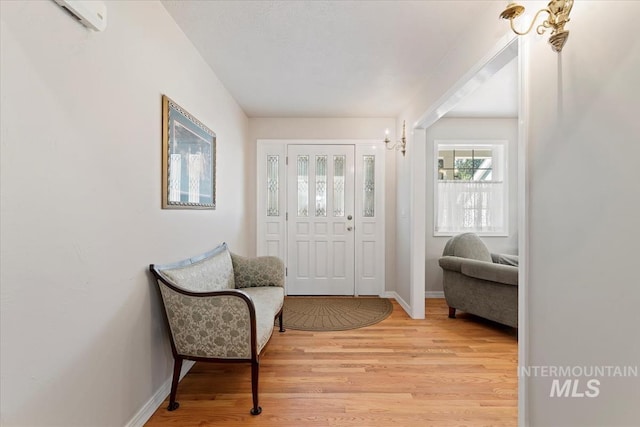 entrance foyer featuring light wood-style flooring, a wall unit AC, baseboards, and a chandelier