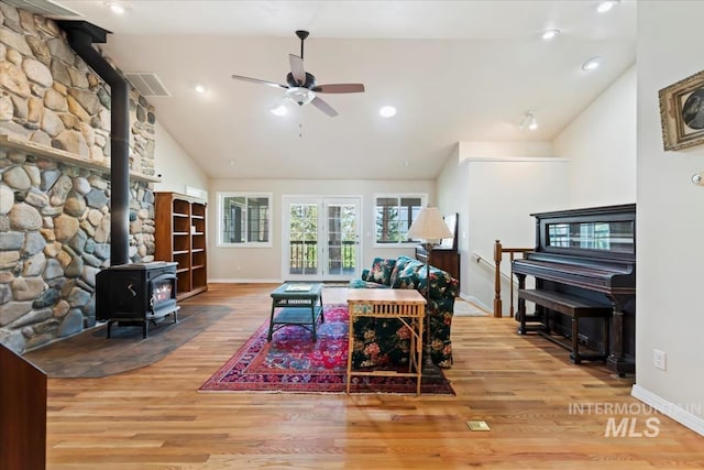 living room featuring high vaulted ceiling, baseboards, ceiling fan, wood finished floors, and a wood stove