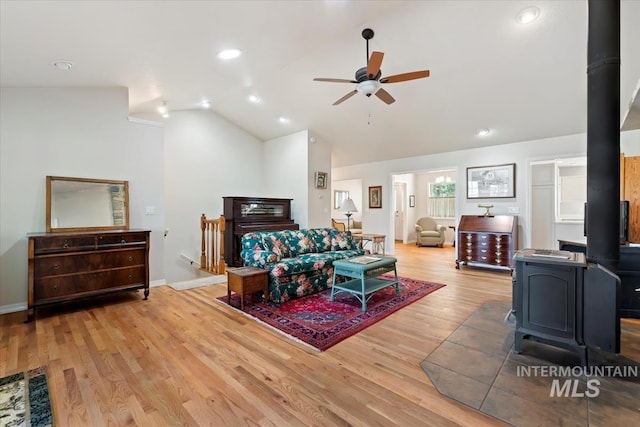 living room featuring light wood finished floors, a wood stove, lofted ceiling, baseboards, and ceiling fan