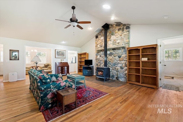 living area with baseboards, wood finished floors, a wood stove, and a ceiling fan