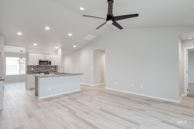 kitchen with stainless steel microwave, backsplash, white cabinetry, a ceiling fan, and a kitchen island with sink