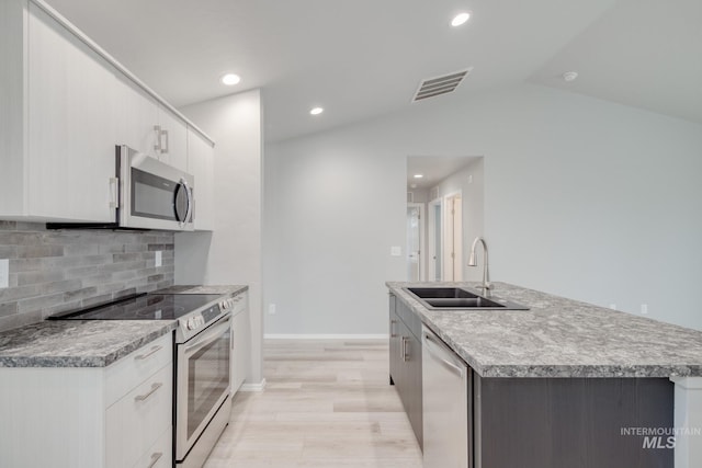 kitchen with lofted ceiling, a kitchen island with sink, a sink, decorative backsplash, and stainless steel appliances