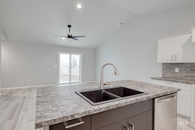 kitchen with a sink, backsplash, stainless steel dishwasher, light countertops, and vaulted ceiling