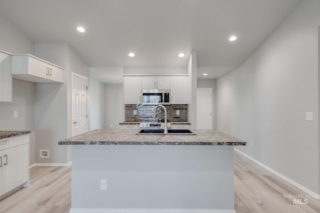 kitchen featuring a sink, stainless steel microwave, tasteful backsplash, and white cabinetry