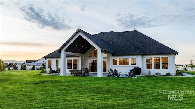 8848 Overunder Ln, Middleton, ID 83644 - back of house at dusk with a yard, a patio, a shingled roof, and stucco siding