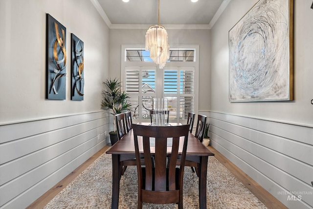 dining room with wood finished floors, a wainscoted wall, crown molding, and an inviting chandelier