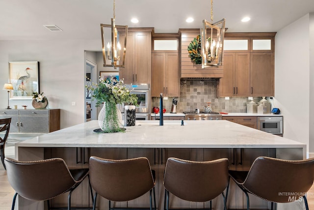 kitchen featuring a center island with sink, a notable chandelier, visible vents, decorative backsplash, and stove