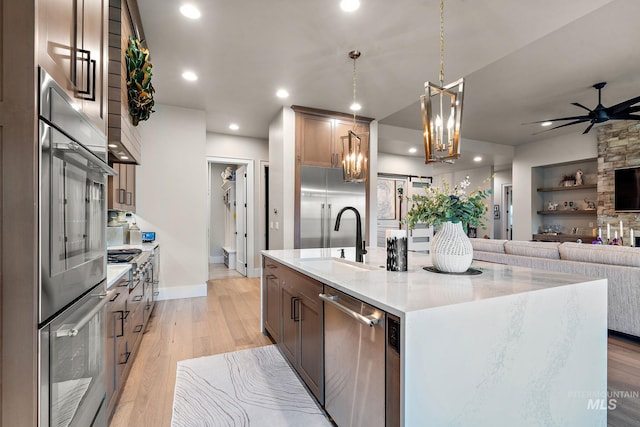 kitchen featuring ceiling fan, light stone counters, a sink, appliances with stainless steel finishes, and light wood finished floors