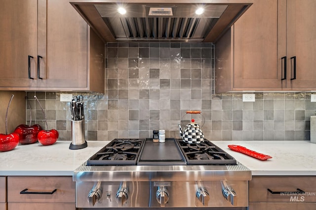 kitchen featuring wall chimney exhaust hood, stainless steel gas stovetop, light countertops, and decorative backsplash