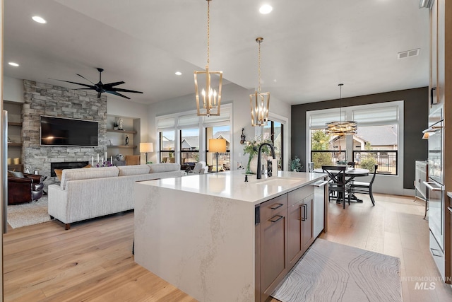 kitchen featuring a stone fireplace, a sink, visible vents, light countertops, and light wood finished floors