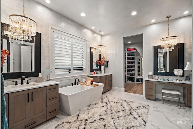 bathroom with an inviting chandelier, marble finish floor, a freestanding tub, and a sink