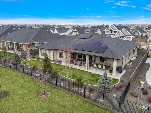 back of house with a fenced backyard, a lawn, a residential view, roof mounted solar panels, and a patio area