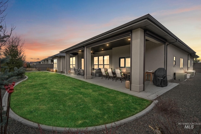 rear view of property featuring a patio, fence, a lawn, and stucco siding