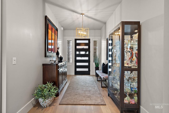 entryway featuring plenty of natural light, baseboards, a notable chandelier, and light wood finished floors